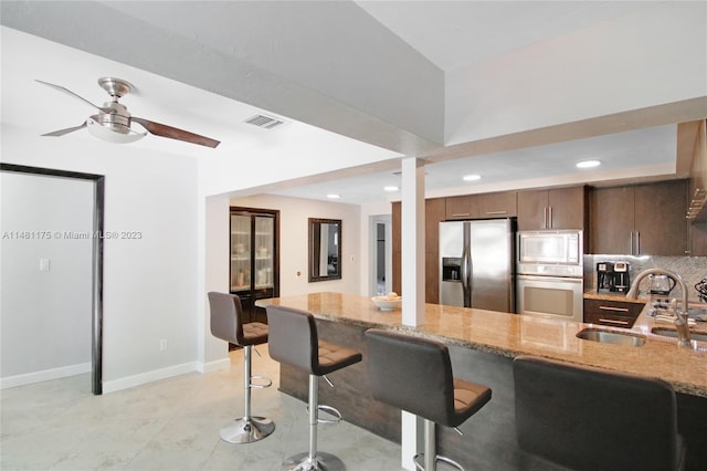 kitchen with ceiling fan, sink, light tile floors, light stone counters, and appliances with stainless steel finishes