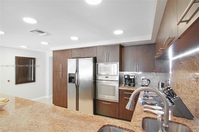 kitchen featuring sink, stainless steel appliances, light stone counters, dark brown cabinets, and tasteful backsplash