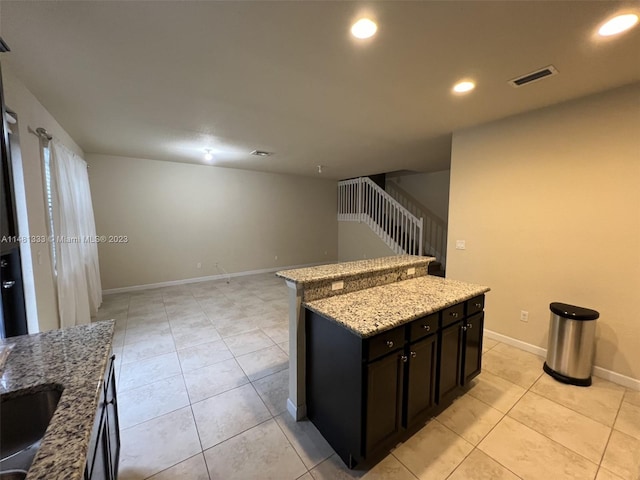 kitchen with a kitchen island, light stone countertops, sink, and light tile flooring