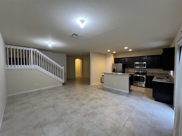 kitchen featuring sink, stainless steel appliances, light tile flooring, and an island with sink