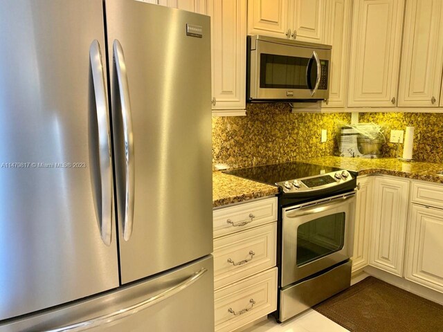 kitchen featuring light tile floors, tasteful backsplash, appliances with stainless steel finishes, white cabinets, and dark stone countertops