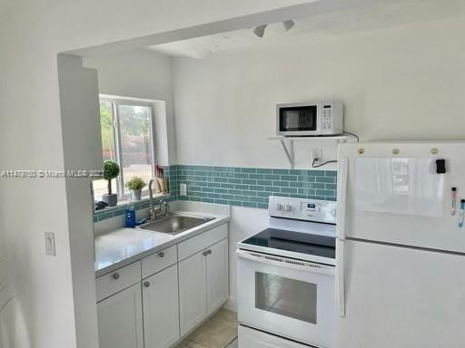 kitchen with white appliances, backsplash, light tile floors, sink, and white cabinets