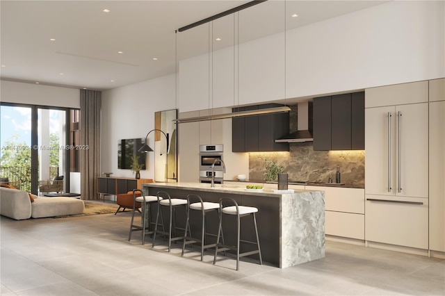 kitchen with light stone countertops, white cabinetry, a kitchen island with sink, a breakfast bar, and wall chimney range hood