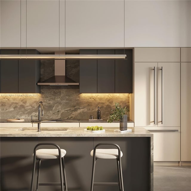 kitchen with a kitchen bar, backsplash, wall chimney exhaust hood, and light stone counters