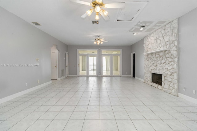 unfurnished living room featuring french doors, a stone fireplace, light tile patterned floors, and ceiling fan