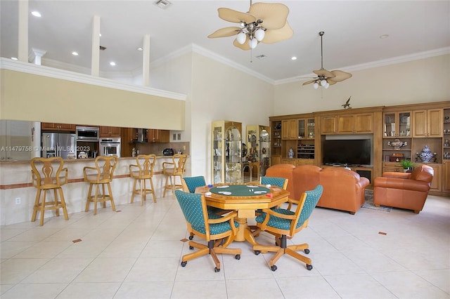 dining room with crown molding, ceiling fan, light tile floors, and a high ceiling