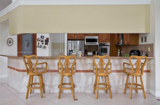 kitchen featuring stainless steel appliances, light tile floors, kitchen peninsula, a breakfast bar area, and crown molding