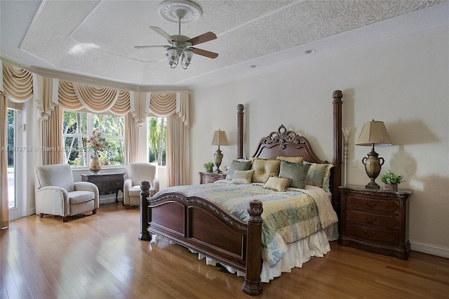 bedroom with ceiling fan, a raised ceiling, access to outside, a textured ceiling, and light wood-type flooring