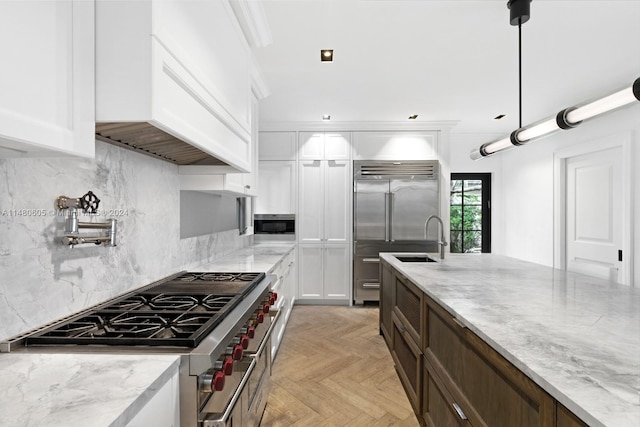 kitchen with premium appliances, white cabinets, light parquet flooring, decorative backsplash, and decorative light fixtures