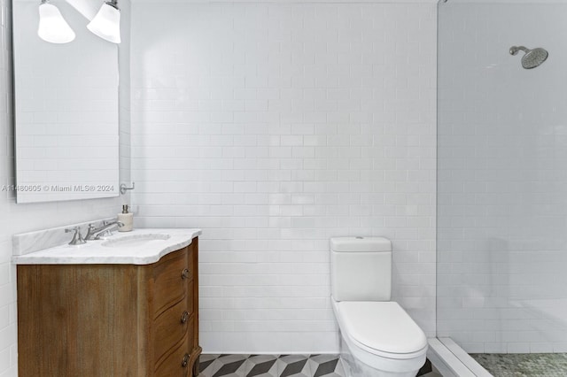 bathroom with tiled shower, vanity, tile walls, toilet, and tile patterned flooring