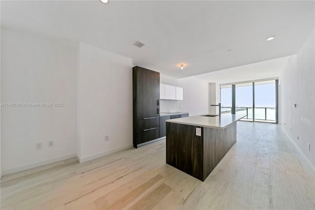 kitchen with white cabinetry, sink, light hardwood / wood-style flooring, a center island with sink, and dark brown cabinets