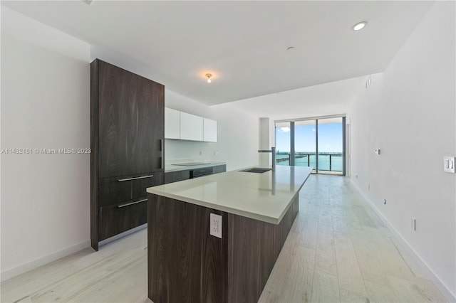 kitchen with light hardwood / wood-style flooring, white cabinets, floor to ceiling windows, a center island with sink, and dark brown cabinetry