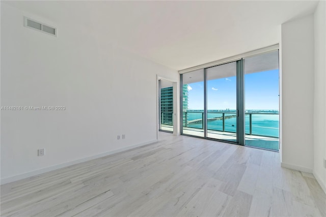 unfurnished room with floor to ceiling windows, a water view, and light hardwood / wood-style flooring