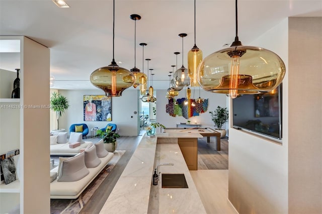 kitchen featuring sink, light stone counters, hanging light fixtures, light hardwood / wood-style floors, and pool table