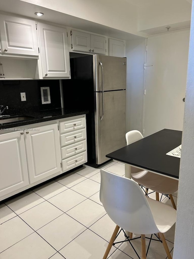 kitchen with light tile flooring, stainless steel refrigerator, white cabinetry, sink, and tasteful backsplash