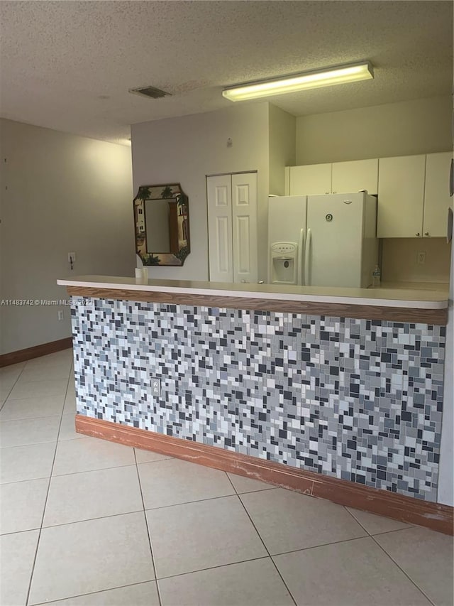 kitchen with light tile floors, a textured ceiling, white fridge with ice dispenser, and white cabinetry