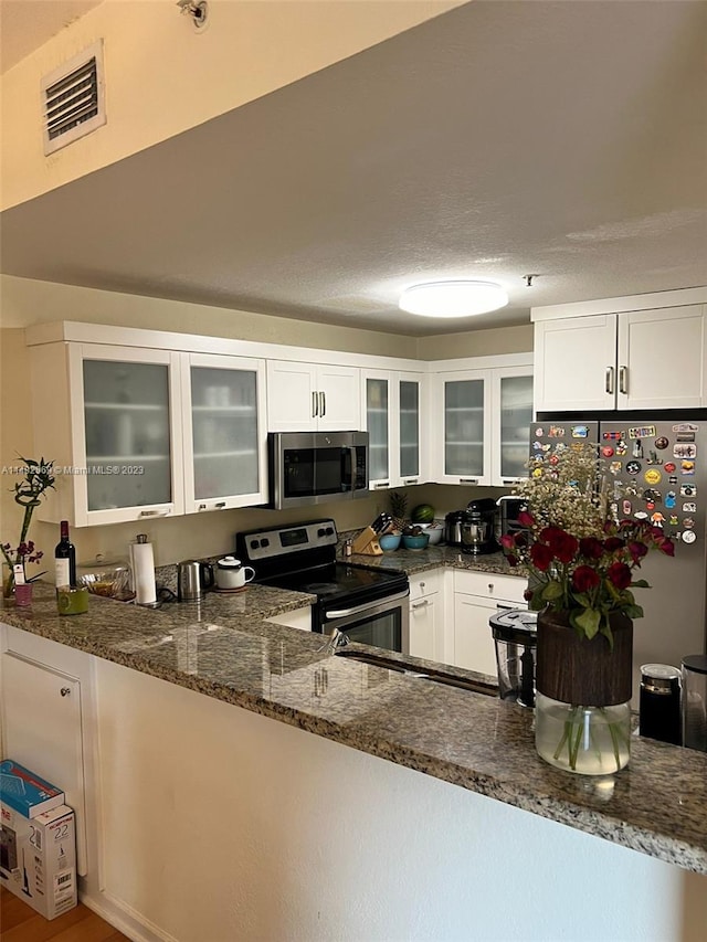 kitchen featuring white cabinets, kitchen peninsula, appliances with stainless steel finishes, and dark stone counters