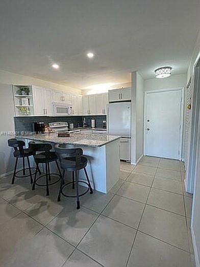 kitchen featuring white cabinets, kitchen peninsula, a kitchen bar, white appliances, and backsplash