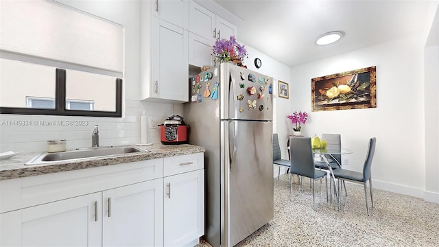 kitchen with sink, stainless steel fridge, white cabinets, light stone countertops, and decorative backsplash