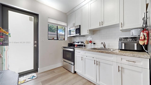 kitchen with stainless steel appliances, light stone counters, decorative backsplash, sink, and white cabinetry