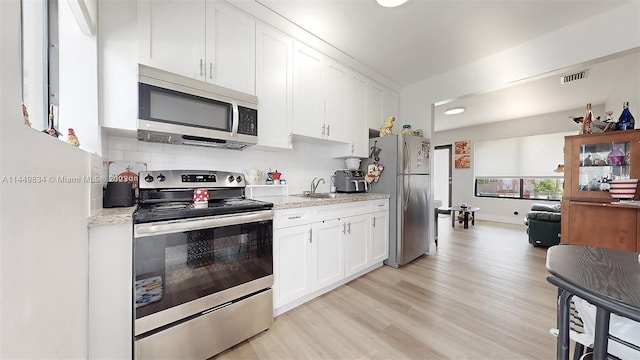 kitchen featuring appliances with stainless steel finishes, light hardwood / wood-style floors, white cabinets, light stone countertops, and decorative backsplash