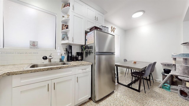 kitchen with white cabinetry, stainless steel refrigerator, sink, tasteful backsplash, and light stone counters