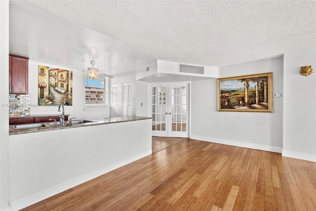 interior space with french doors, light hardwood / wood-style flooring, sink, dark stone counters, and ceiling fan