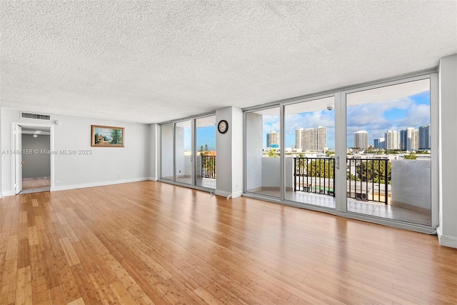 spare room with floor to ceiling windows, a healthy amount of sunlight, light wood-type flooring, and a textured ceiling