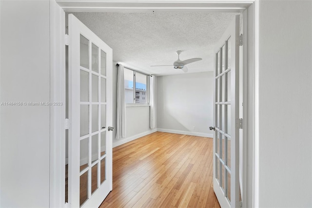 hall with french doors, light hardwood / wood-style flooring, and a textured ceiling