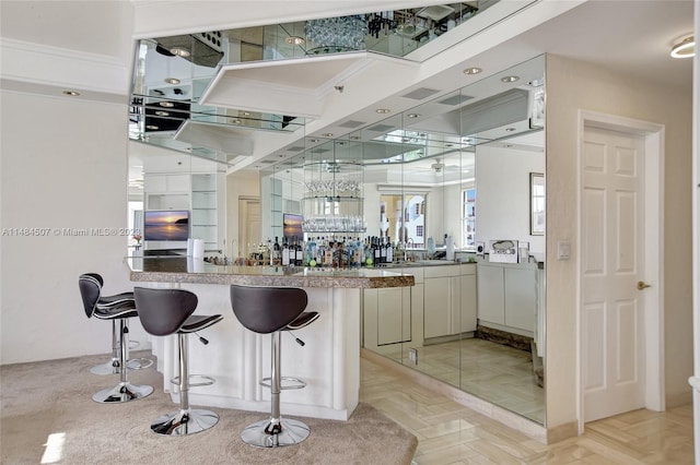 bar with crown molding, white cabinets, and light parquet floors