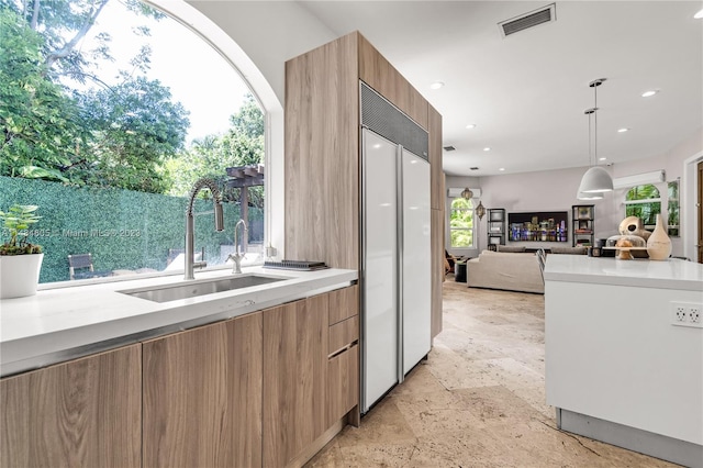 kitchen featuring light tile floors, decorative light fixtures, paneled built in fridge, a healthy amount of sunlight, and sink