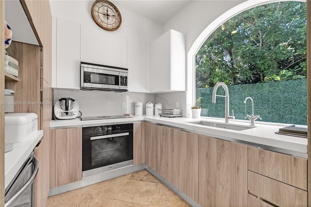 kitchen featuring black oven, white cabinets, backsplash, and sink