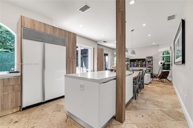 kitchen with light tile floors, decorative light fixtures, paneled fridge, a wealth of natural light, and a center island with sink