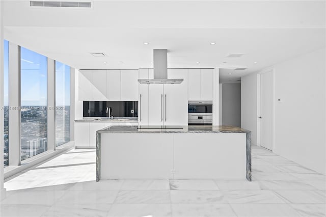 kitchen with white cabinetry, island range hood, expansive windows, and dark stone counters