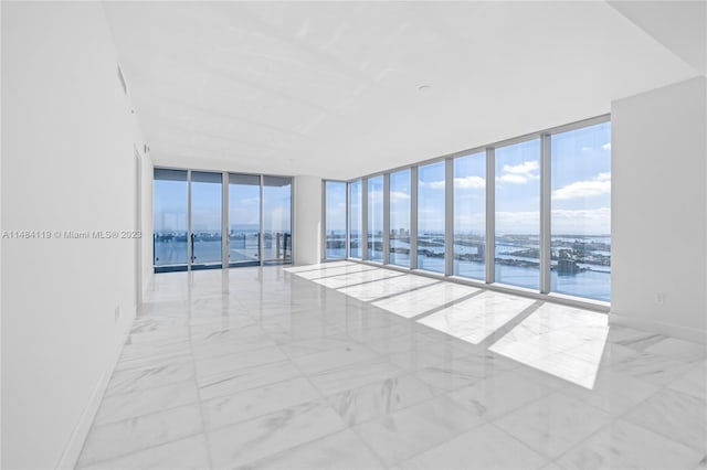 spare room featuring a water view, a wall of windows, and a healthy amount of sunlight