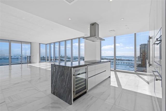 kitchen featuring a water view, expansive windows, white cabinets, island exhaust hood, and beverage cooler