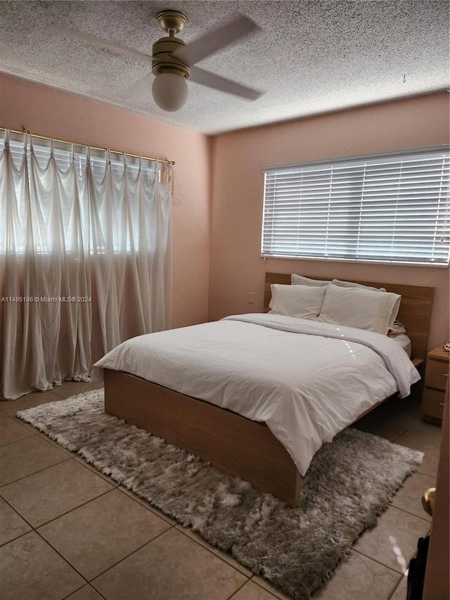 tiled bedroom with ceiling fan and a textured ceiling