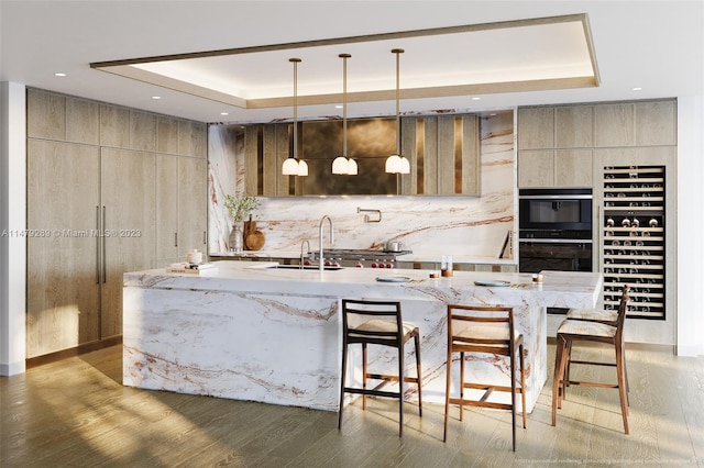 kitchen with black double oven, a kitchen bar, light wood-type flooring, a center island with sink, and pendant lighting