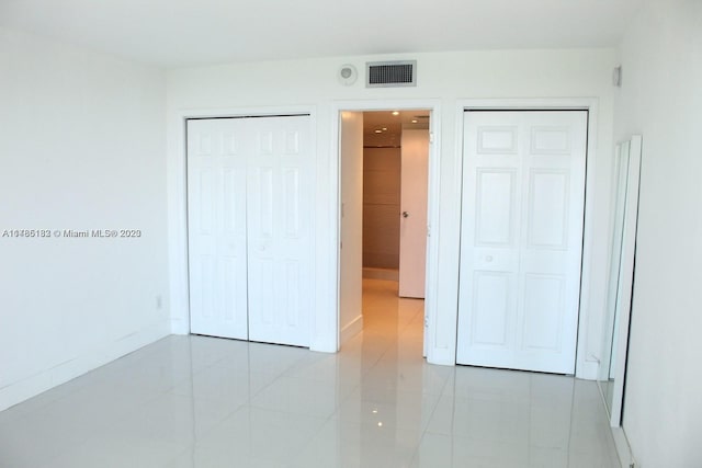 unfurnished bedroom with multiple closets and light tile floors