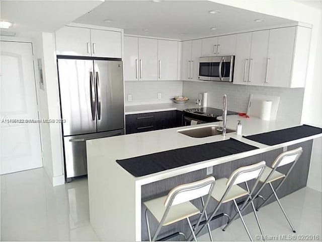 kitchen with light tile floors, tasteful backsplash, appliances with stainless steel finishes, white cabinetry, and sink