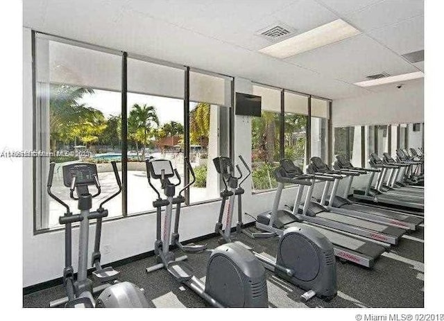 gym with a paneled ceiling and dark colored carpet