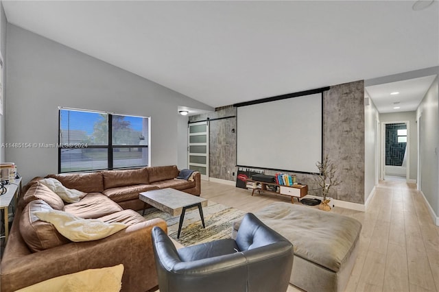 cinema featuring a barn door, lofted ceiling, and light hardwood / wood-style flooring