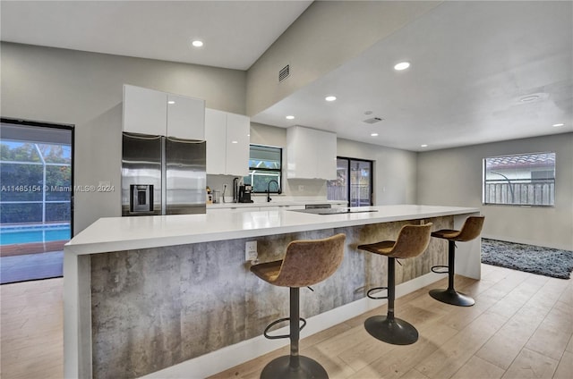 kitchen featuring a breakfast bar, white cabinetry, light hardwood / wood-style floors, and stainless steel fridge