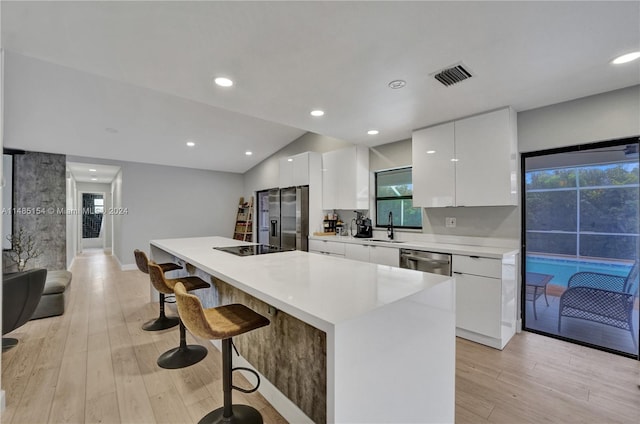 kitchen with light hardwood / wood-style floors, a kitchen island, stainless steel appliances, a kitchen bar, and white cabinets