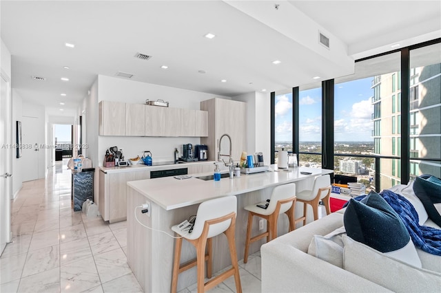 kitchen featuring floor to ceiling windows, light brown cabinetry, a kitchen island with sink, and a kitchen breakfast bar