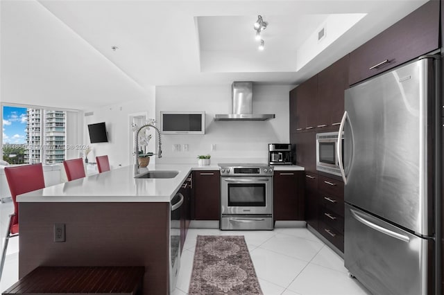 kitchen featuring appliances with stainless steel finishes, sink, light tile floors, wall chimney exhaust hood, and dark brown cabinetry