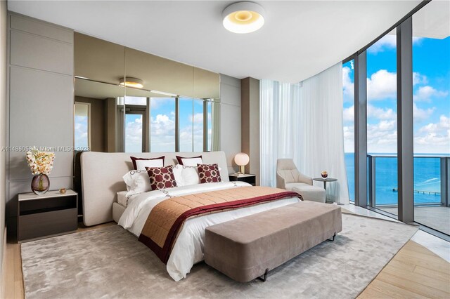 bedroom featuring a water view, expansive windows, access to outside, and light hardwood / wood-style flooring