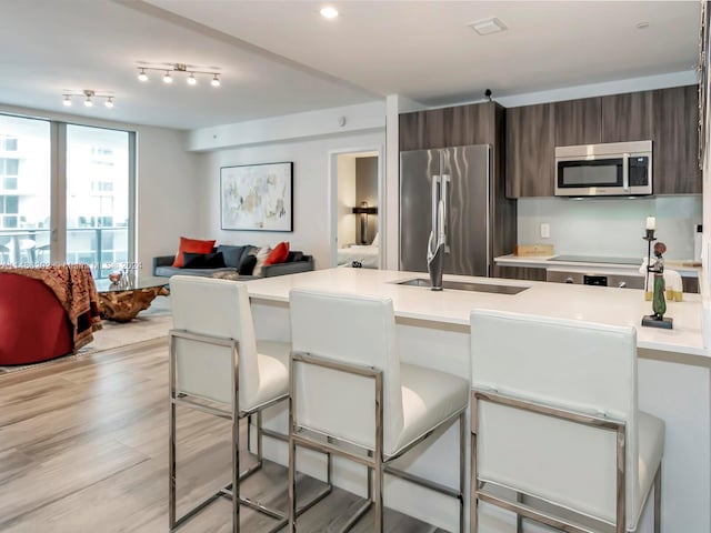 kitchen with dark brown cabinetry, sink, appliances with stainless steel finishes, a breakfast bar, and light wood-type flooring