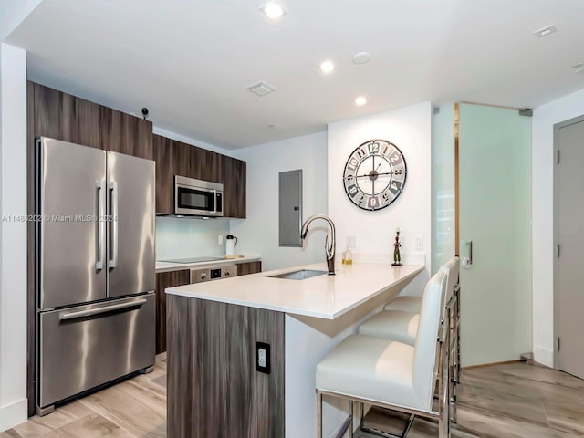 kitchen featuring sink, kitchen peninsula, light hardwood / wood-style flooring, appliances with stainless steel finishes, and a kitchen bar