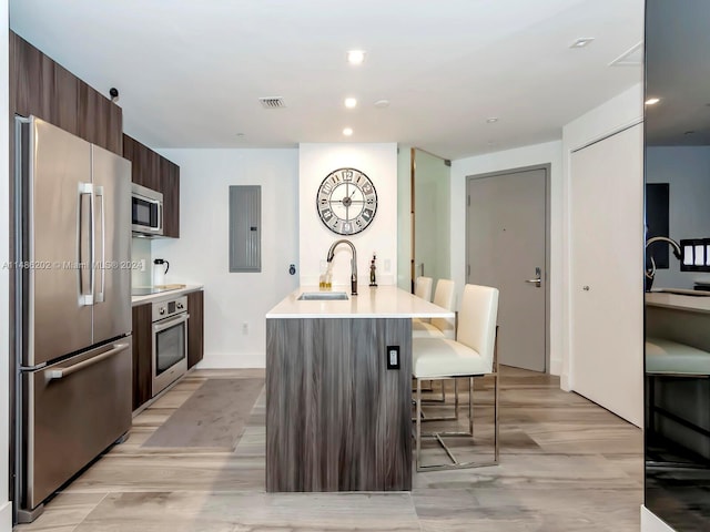 kitchen featuring appliances with stainless steel finishes, a breakfast bar, light wood-type flooring, a center island with sink, and sink